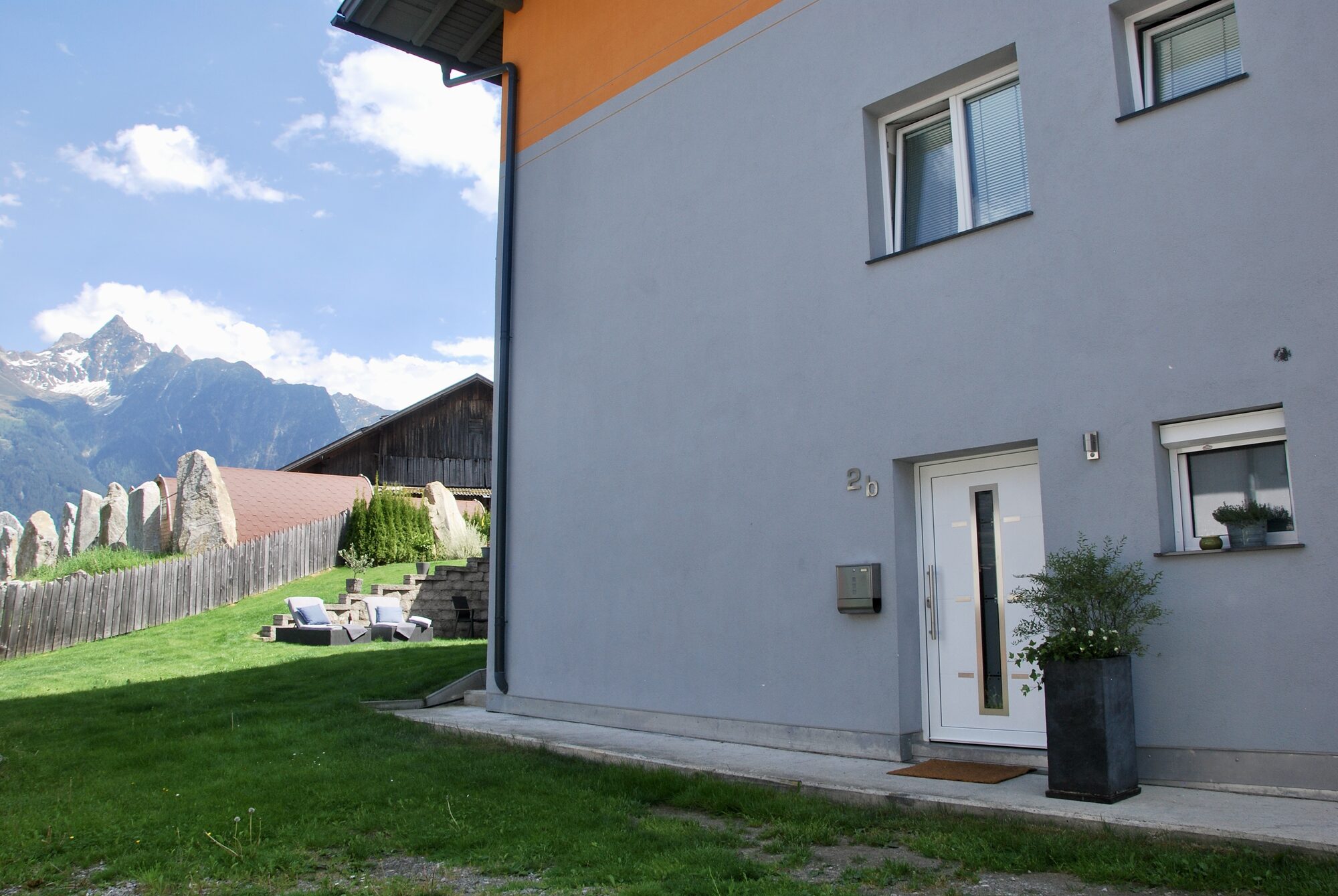 Das Haus Süta von außen, mit Garten und Bergen im Hintergrund.