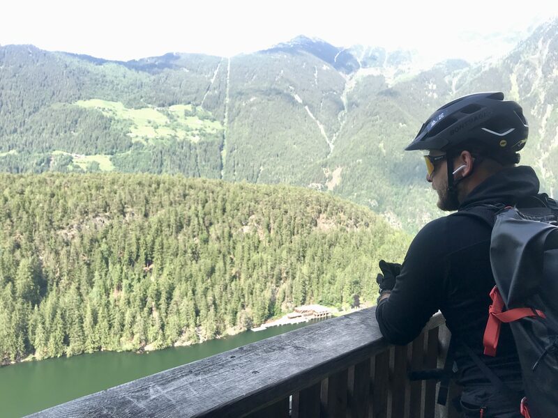 Blick von einer Aussichtsplattform über den bewaldeten Hang auf einen See im Tal.